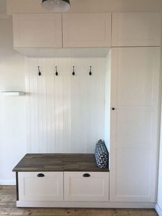 an empty room with white cupboards and wooden bench in the center, along with hooks on the wall