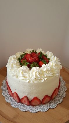 a cake with white frosting and fresh strawberries on top is sitting on a wooden table