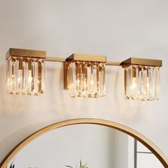 three lights on the wall above a mirror and potted plant in front of it