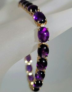 Beautiful bracelet! Marked 14K yellow gold amethyst cabochon cut gemstone bracelet. The 14K yellow gold bracelet is set with nineteen oval shaped cabochon cut amethyst gemstones. Each amethyst measures approximately 8.00 mm x 6.50 mm for an approximate total amethyst weight of 23.75 carats. The amethyst set in the bracelet are well matched in a fine quality and color. The amethyst display a vivid purple color with red flash. The 14K yellow gold amethyst bracelet has a solid and secure 14K yellow gold clasp with a safety catch. The amethyst bracelet measures approximately 7 1/4 inches long. The 14K yellow gold amethyst bracelet weighs 15.00 grams.   The amethyst bracelet comes in a quality bracelet box.  You can feel secure knowing that the 14K yellow gold amethyst bracelet was professional Fine Jewelry Bracelet With Cabochon, Luxury Purple Cabochon Jewelry, Formal Amethyst Oval Cabochon Jewelry, Elegant Cabochon Amethyst Gemstones, Formal Amethyst Jewelry, Oval Cabochon, Elegant Amethyst Cabochon Gemstones, Formal Purple Cabochon Gemstones, Oval Cabochon Bracelets For Formal Occasions, Luxury Oval Amethyst Jewelry