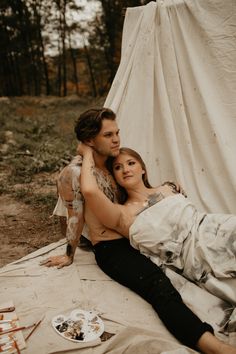 a man and woman laying on the ground in front of a white tarp covered tent