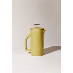 a yellow coffee pot with a wooden handle and lid on a white surface, in front of a plain background