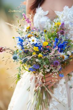 a bride holding a bouquet of wildflowers and grasses in her hands, outdoors