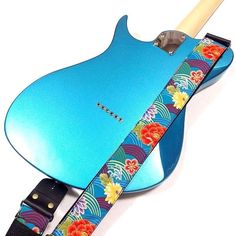 a blue guitar strap with flowers on it and a wooden pickle in the back