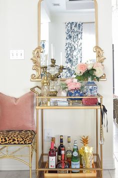 a gold bar cart filled with liquor bottles and flowers in front of a large mirror