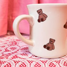 a white coffee cup with brown teddy bears painted on it's side sitting on a doily