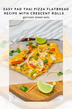 a pizza with cheese and vegetables on it sitting on a cutting board next to a lime slice