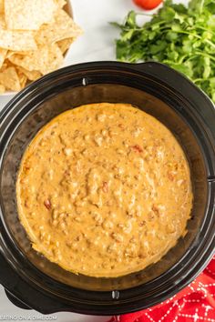 a crock pot filled with salsa and tortilla chips next to fresh vegetables