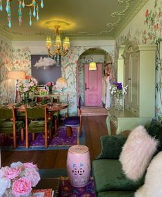 a living room filled with lots of furniture and flowers on the wall next to a pink door