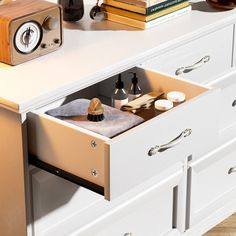 an open drawer in a white cabinet with books and other items on the table behind it