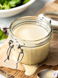 a glass jar filled with cream sitting on top of a wooden cutting board next to a bowl of lettuce