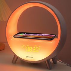 an alarm clock with a cell phone in it on top of a table next to a lamp