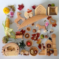 various wooden toys are arranged on a white surface with autumn leaves and other things surrounding them