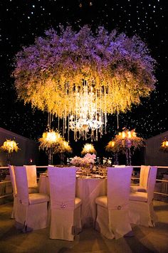 a table with white chairs and chandelier hanging from it's centerpiece