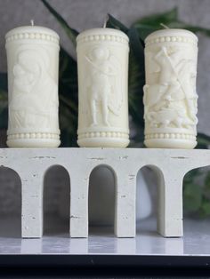 three white candles sitting on top of a shelf