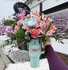 a person holding up a cup with flowers in it on the side of a building