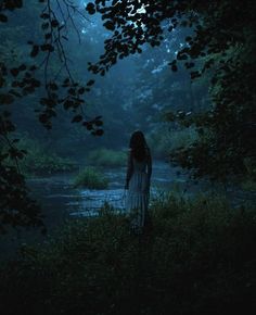 a woman standing in the woods at night with her back turned to the camera, looking down