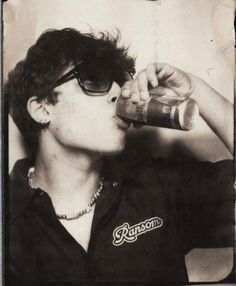 black and white photograph of a man drinking from a can with sunglasses on his head