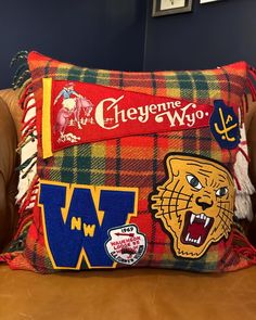 a plaid pillow with some college mascot patches on it, sitting on a leather chair