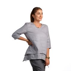 a woman standing with her hands on her hips and wearing a gray top that has an asymmetrically shaped neckline