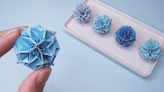 someone is holding three origami flowers in front of a white tray with blue paper on it