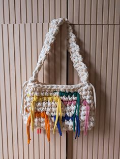 a crocheted bag hanging on the wall with colorful tassels attached to it