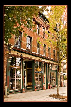 an old brick building on the corner of a street in front of a tree with autumn leaves