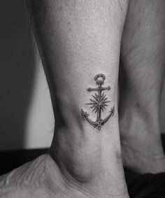 a black and white photo of an anchor with compass tattoo on the side of his foot