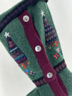 a pair of green knitted stockings with buttons and christmas trees on them, hanging from a hook