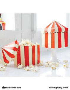 two red and white striped popcorn buckets next to a table with popcorn on it