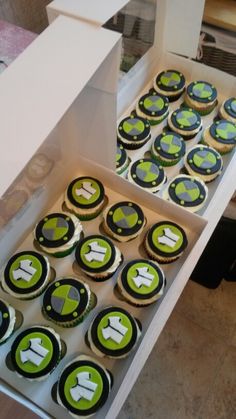 cupcakes with green and black frosting are in a box on the table