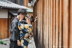 a man and woman standing next to each other in front of a wooden building with wood sidings