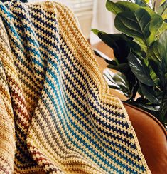 a crocheted blanket sitting on top of a couch next to a potted plant