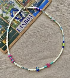 a necklace with multicolored beads is laying on a piece of paper next to a postcard