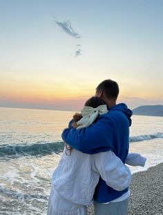 a man and woman hug on the beach as the sun sets