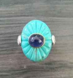 a turquoise ring with a blue stone in the center on a wooden surface, sitting on top of a piece of wood