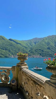 a balcony overlooking the water and mountains with flowers in pots on each railing, along with boats