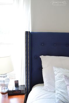 a bed with white pillows and blue headboard next to a window in a bedroom