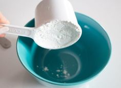 a person is spooning sugar into a blue bowl with a measuring spoon in it