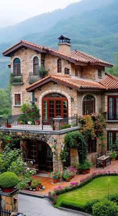 a large house with lots of plants and flowers on the front lawn, surrounded by mountains