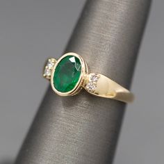 This richly hued ring is just the natural emerald you've been looking for. Sitting low on the finger and well protected by the bezel setting, this emerald glows green. The stone measures 8mm x 6mm, weighing 1.02ct. It is flanked by two round prong set diamonds on the shoulders, just enough sparkle to flash! The diamonds are F/G color and VS clarity, totaling 0.08ctw. The ring is crafted in solid 14k yellow gold and weighs 3.78g. It is currently a size 5.5 and can be resized before shipment for a Bezel Set Diamond, Natural Emerald, Emerald Ring, Bezel Setting, Prong Setting, Statement Rings, Emerald, Flash, Diamonds