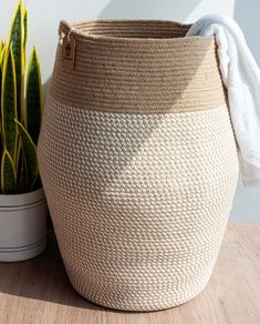 a large woven basket next to a potted plant on a wooden table with a white wall in the background