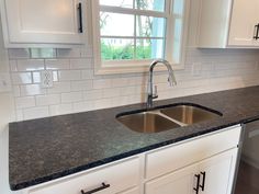 a kitchen with white cabinets and black counter tops, along with a stainless steel sink