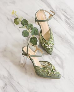 two pairs of green high heels with flowers on them next to a potted plant