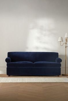 a blue couch sitting on top of a hard wood floor next to a white rug