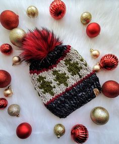 a knitted hat with red and black pom - poms surrounded by christmas ornaments