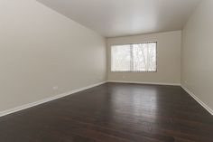 an empty living room with hard wood flooring and large window in the corner on the far wall