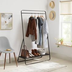 a rack with clothes and shoes hanging on it in front of a window next to a chair