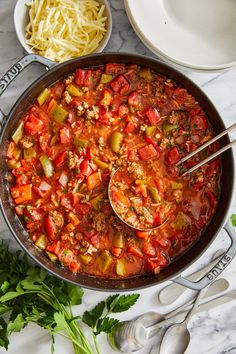 a pan filled with meat and vegetables on top of a table next to silver spoons