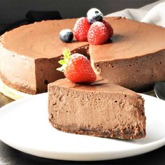 a piece of chocolate cheesecake on a white plate with strawberries and blueberries